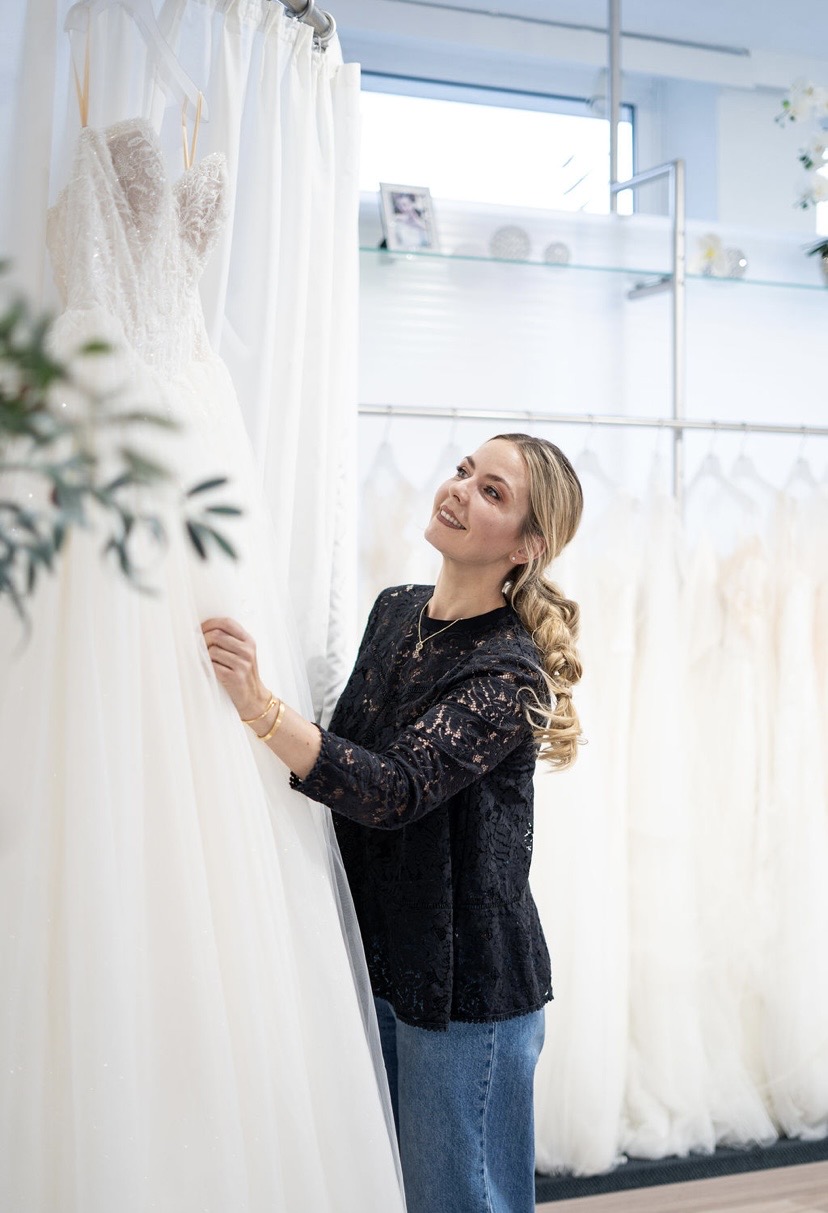 Inhaberin Janna betrachtet lächelnd ein weißes Hochzeitskleid in einem Brautmodengeschäft.